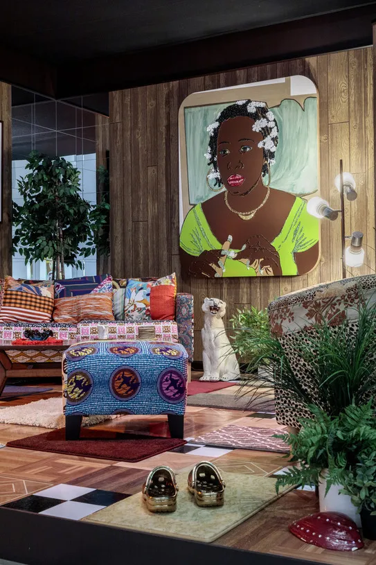 Mickalene Thomas All About Love Exhibition featuring a living room set up with bronze croc sandals, a colorful couch and ottoman, and a painting of a black woman with a green dress