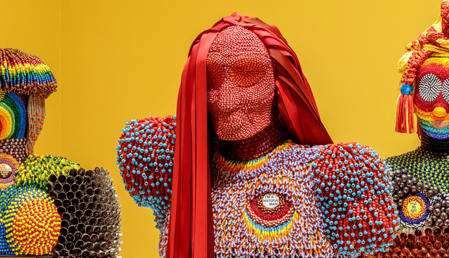 Exhibition photo of beaded figurines on yellow background